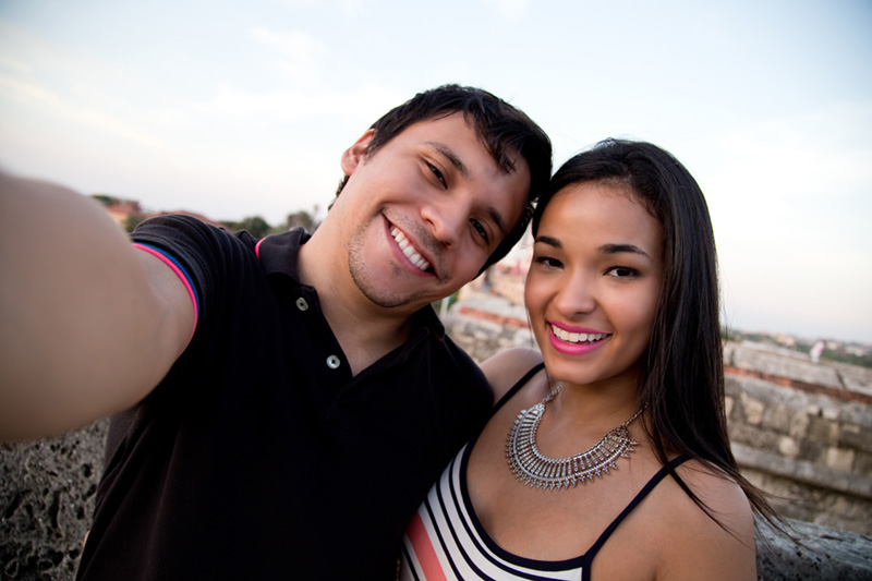 Young couple laying on their backs on pavement looking up at camera with smiles.